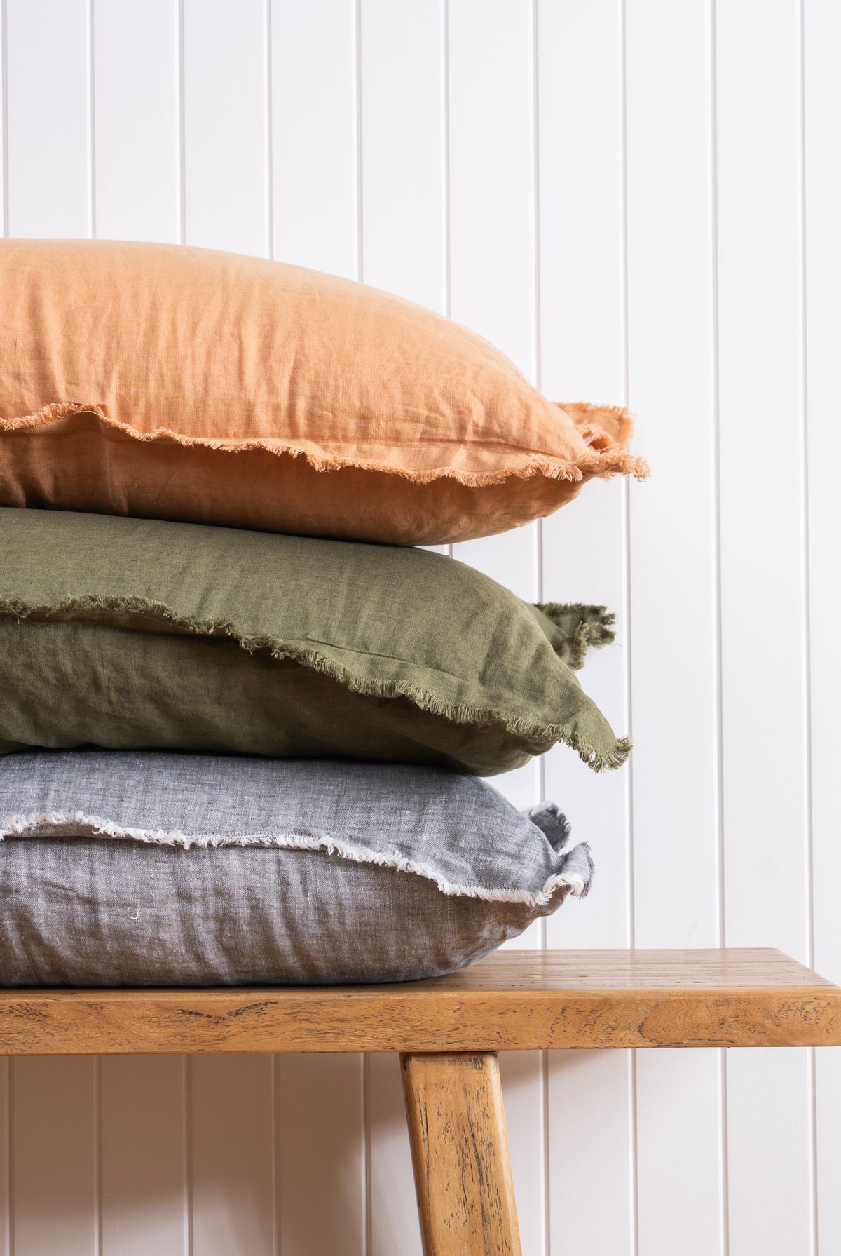 Fringed detail of cushions stacked on bench against which wall