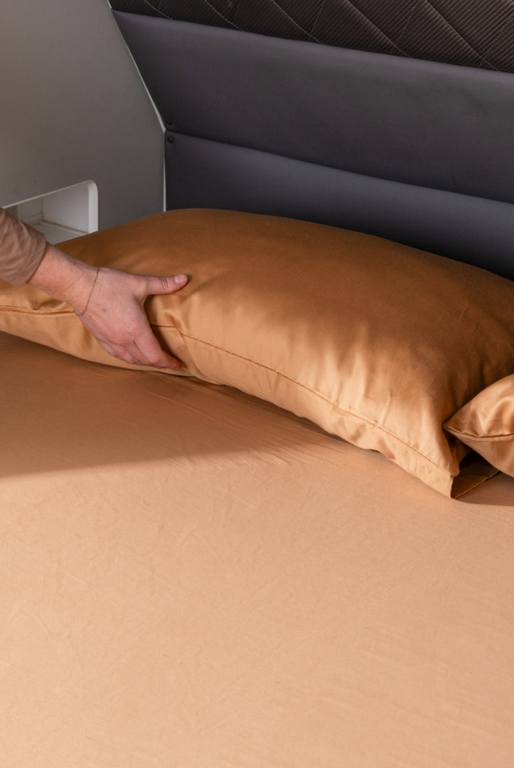 Hand placing a rust pillow on a caravan bed