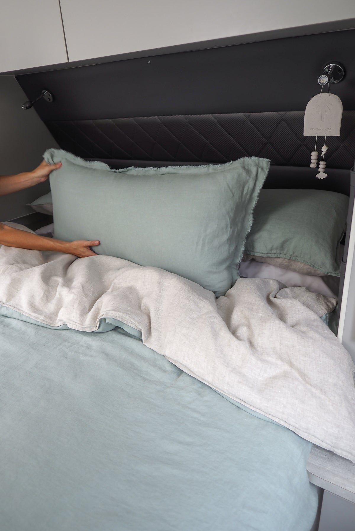 A lumbar cushion in a light color is placed on a bed with a person adjusting it. The cushion appears soft and is part of a bedding set.