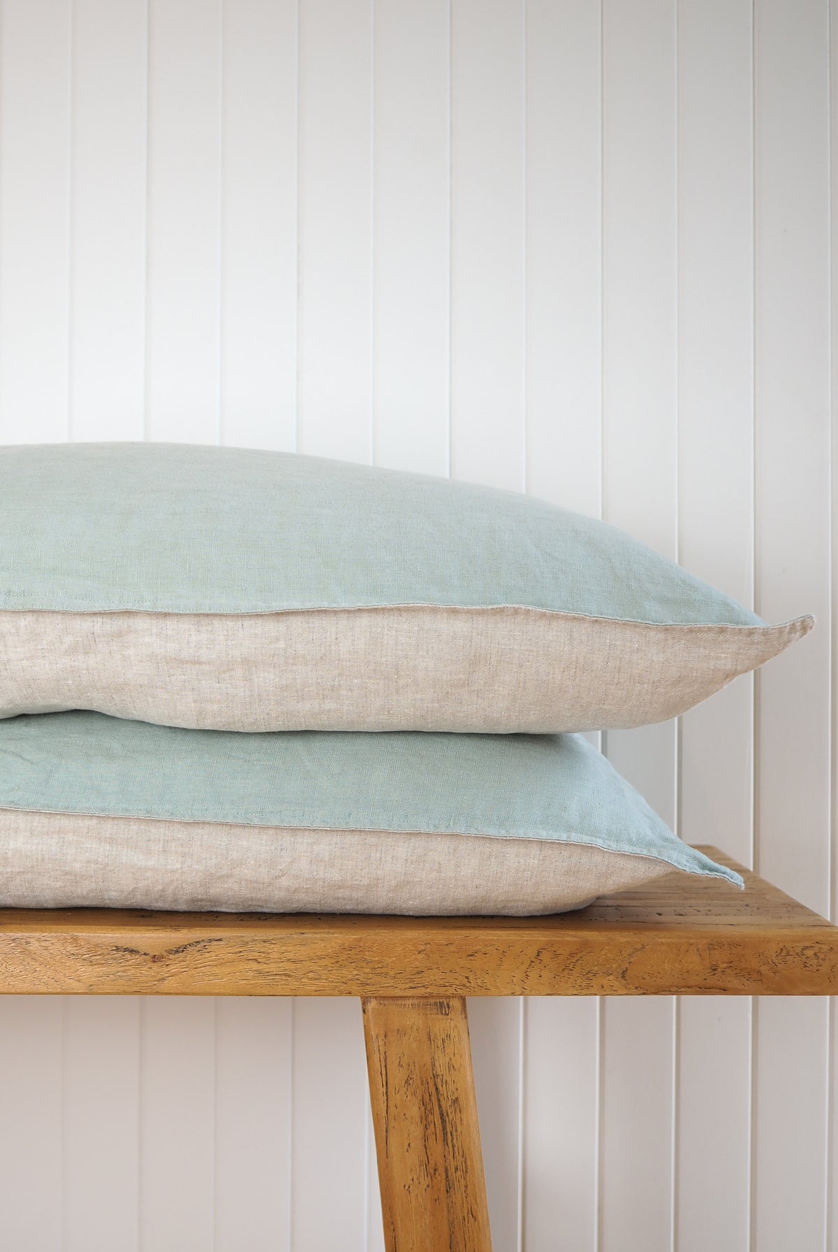 Sage green and oatmeal pillows stacked on a white wall