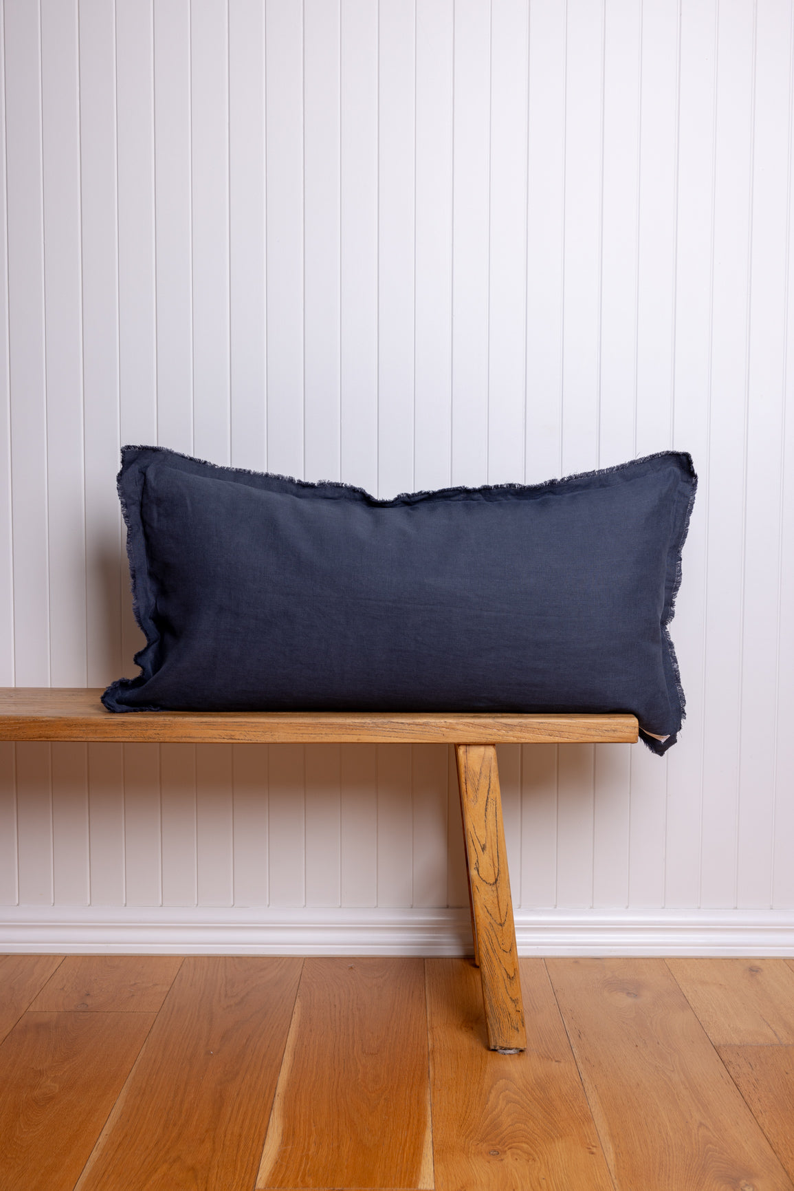 Navy blue pillow on a wooden bench against a white paneled wall.