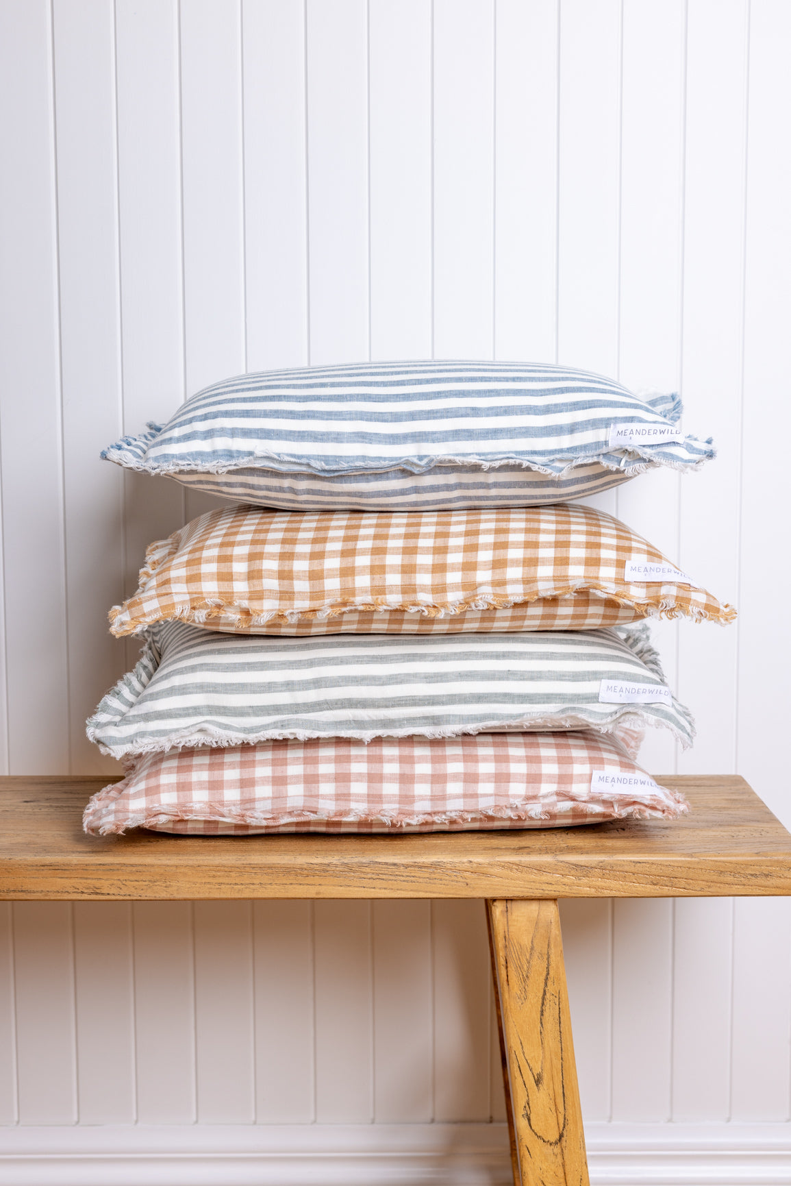 Stack of checkered pillows on a wooden bench against a white paneled wall