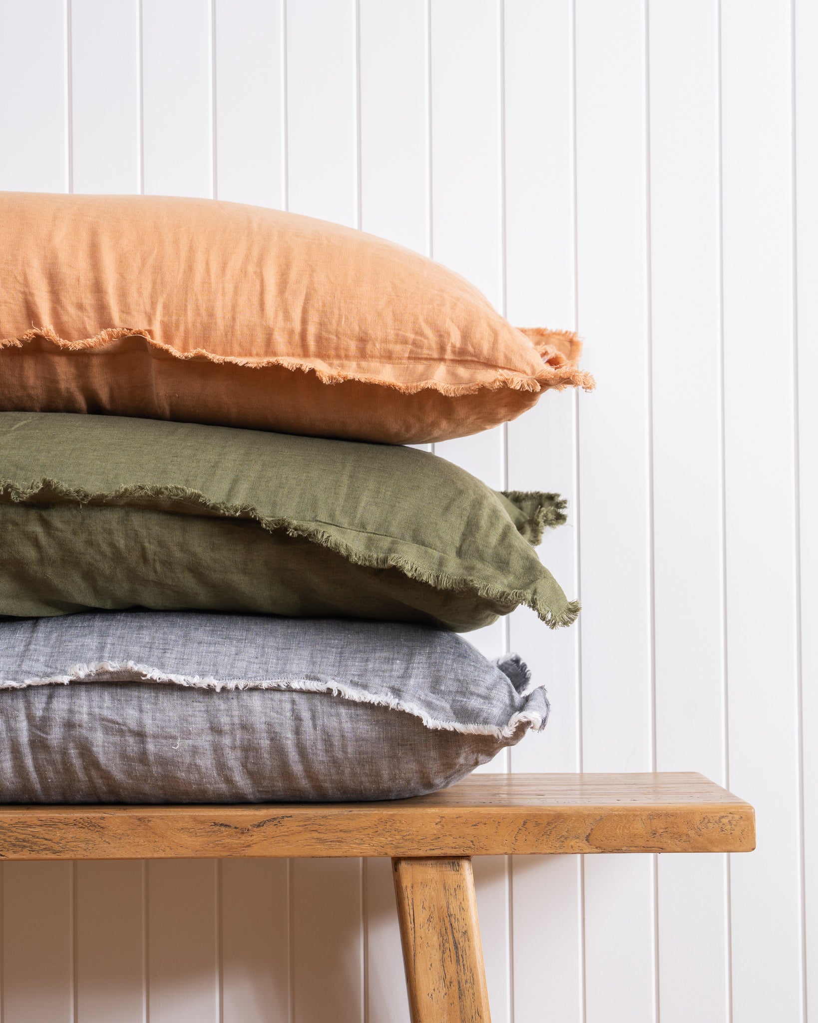 Fringed detail of cushions stacked on bench against which wall