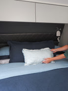 Person arranging pillows on a bed with a striped pillow in a caravan bedroom setting.