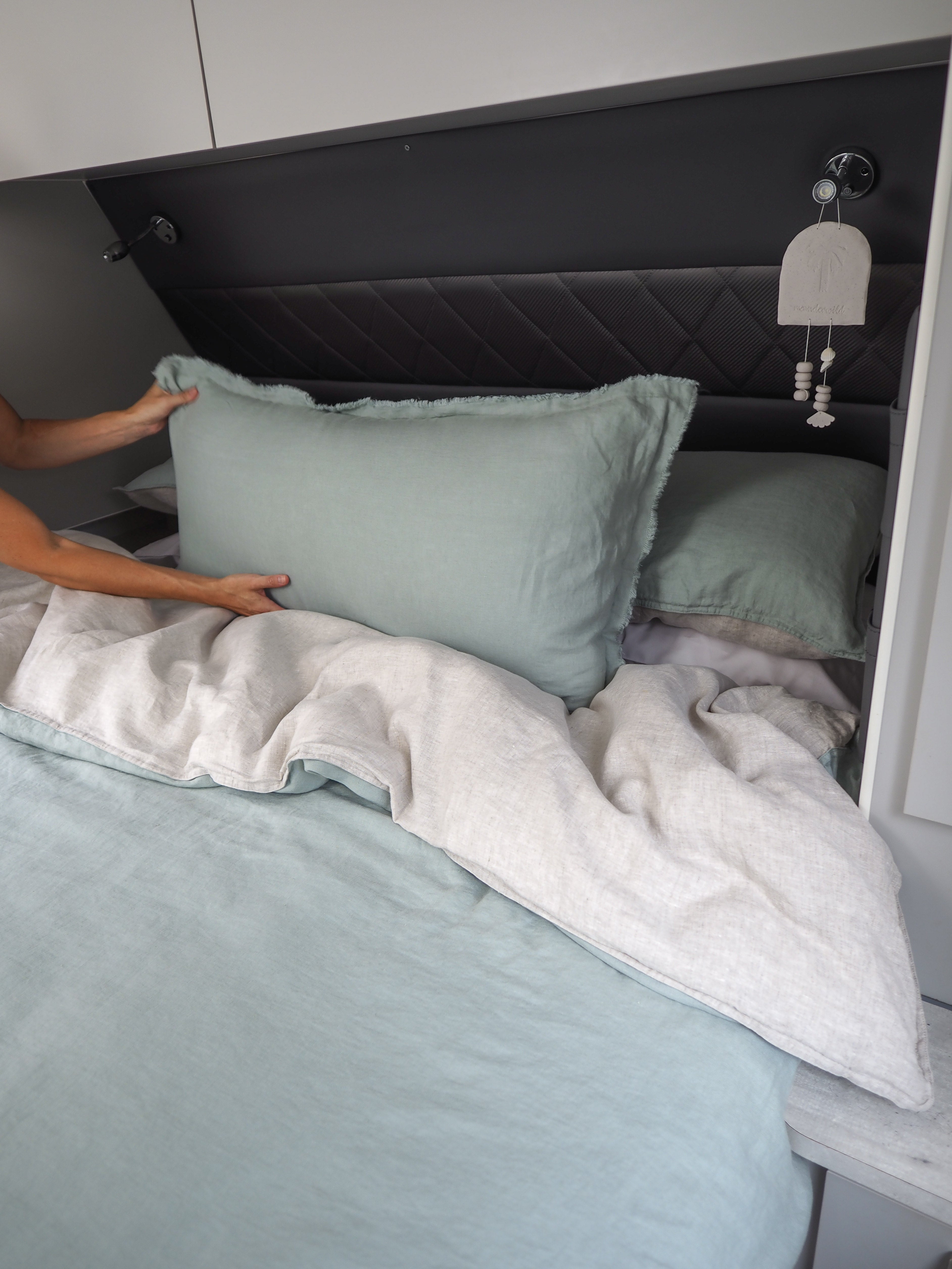 A lumbar cushion in a light color is placed on a bed with a person adjusting it. The cushion appears soft and is part of a bedding set.