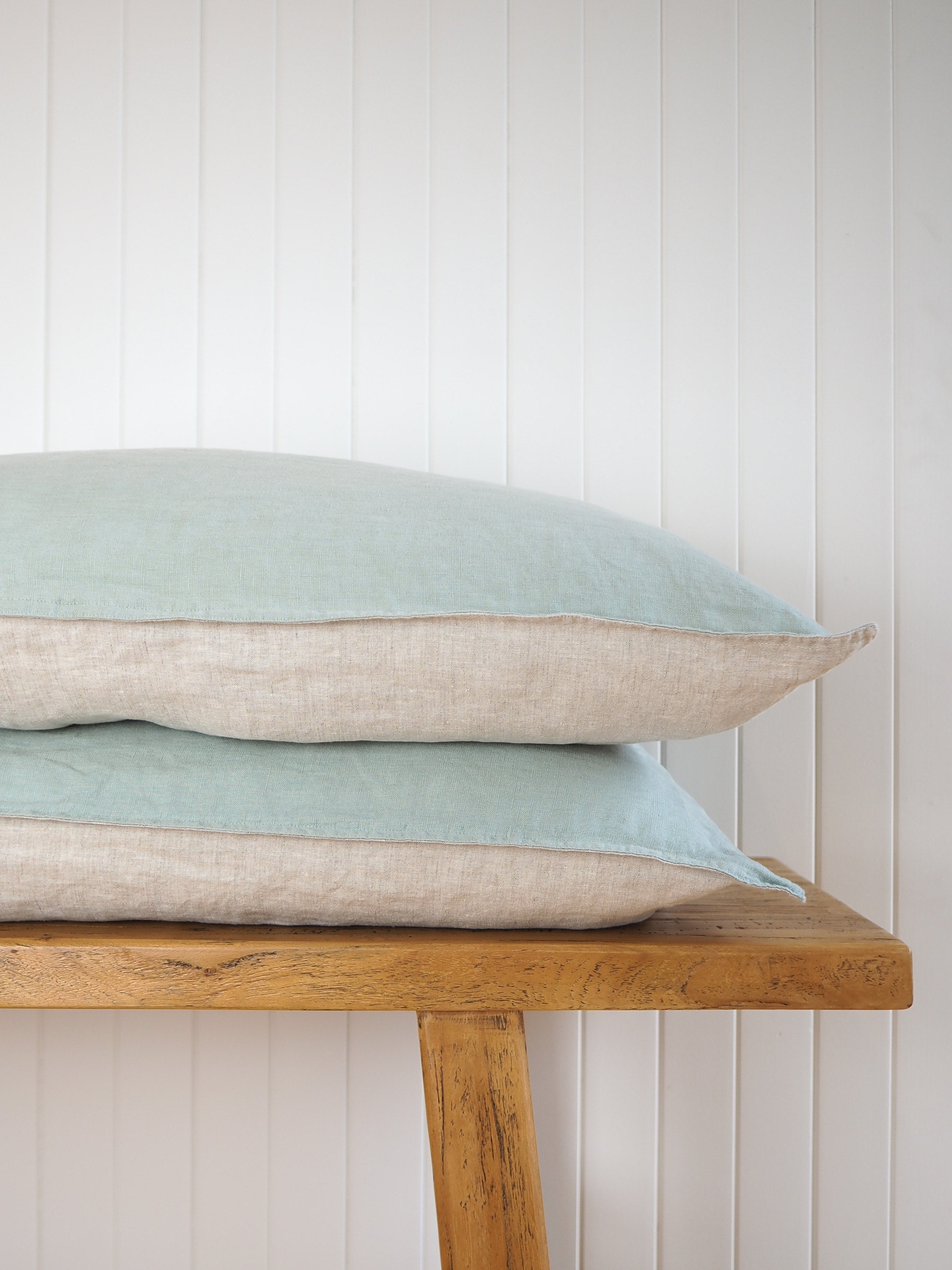 Sage green and oatmeal pillows stacked on a white wall