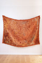 Rusty Orange Cotton Throw with map design hanging on a white wall.